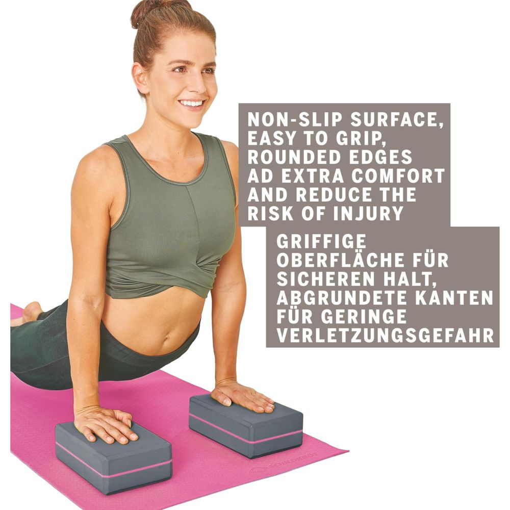 Femme en pose de yoga sur tapis rose, mains sur deux blocs de yoga gris.