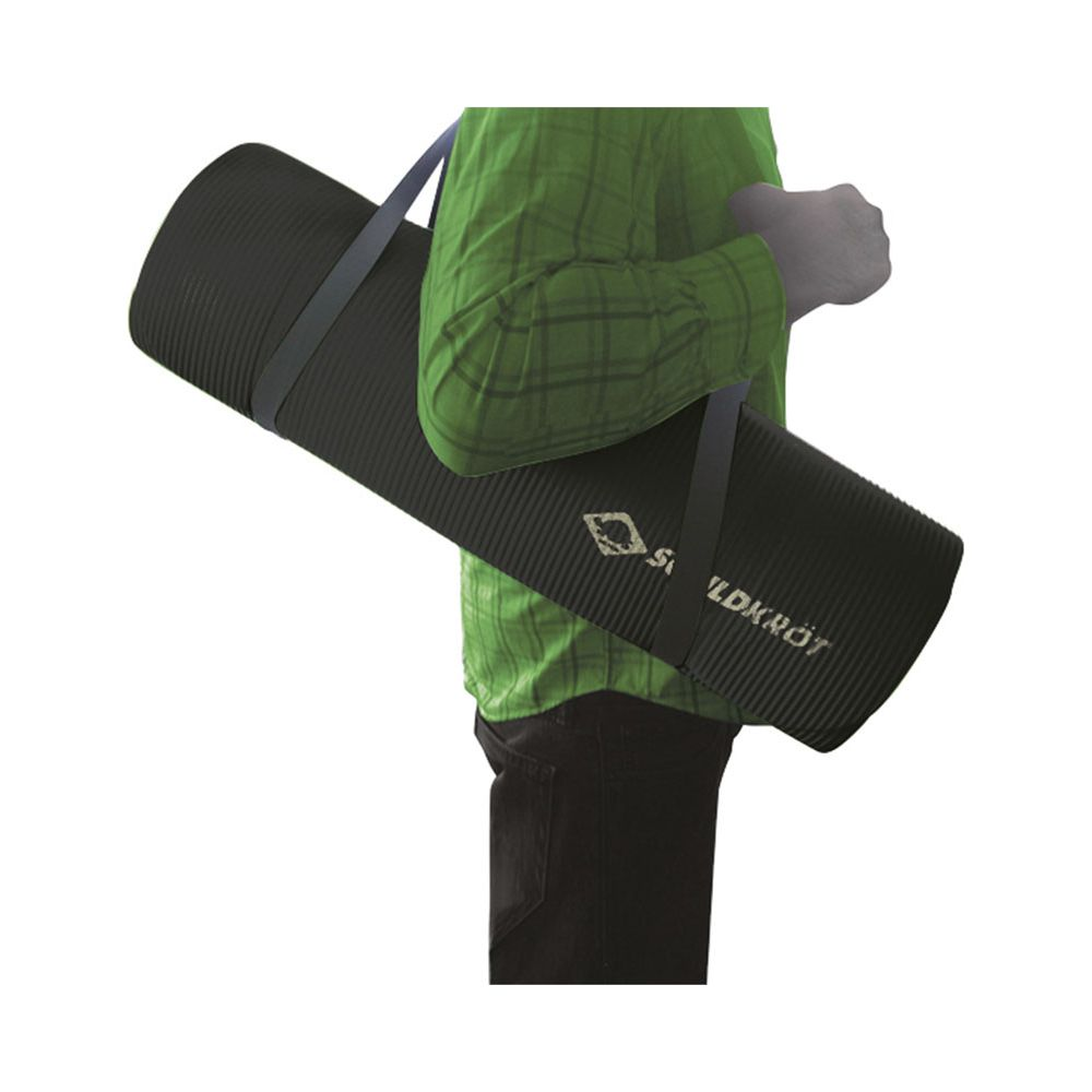 Personne en chemise verte porte un tapis noir enroulé avec des sangles.