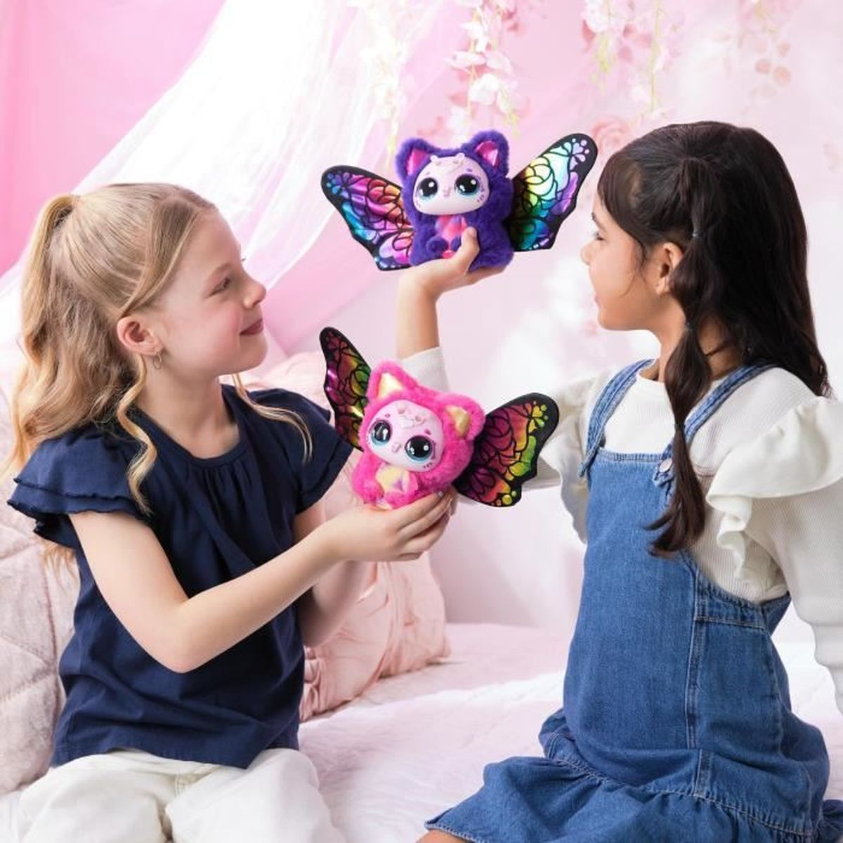 Dos niñas sostienen criaturas de peluche con alas coloridas.