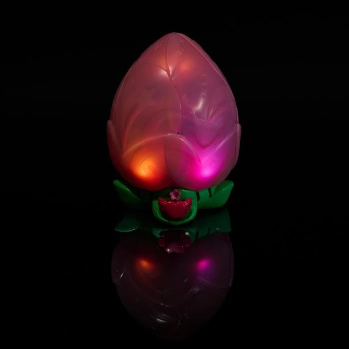 Una luz nocturna de capullo rosa con hojas verdes y reflejo sobre fondo negro.