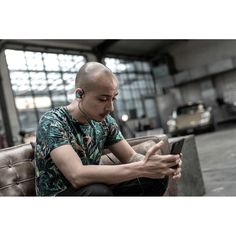 Łysy mężczyzna w słuchawkach siedzi na kanapie i patrzy na telefon.