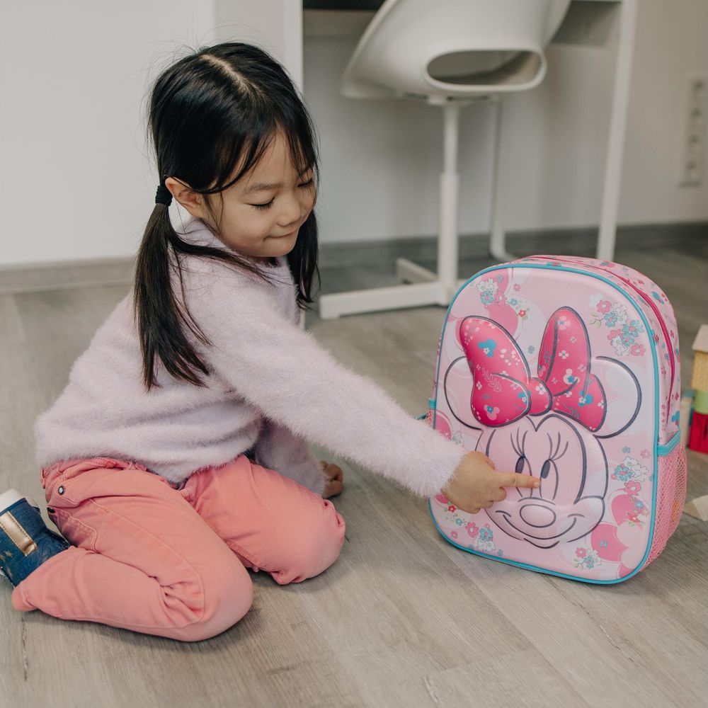 A young girl with pigtails touches a pink Minnie Mouse backpack.