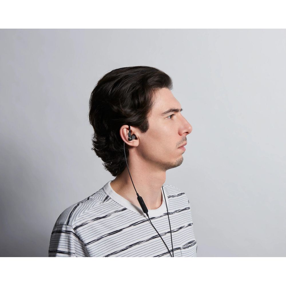 Un homme aux cheveux sombres porte des écouteurs et un t-shirt rayé.