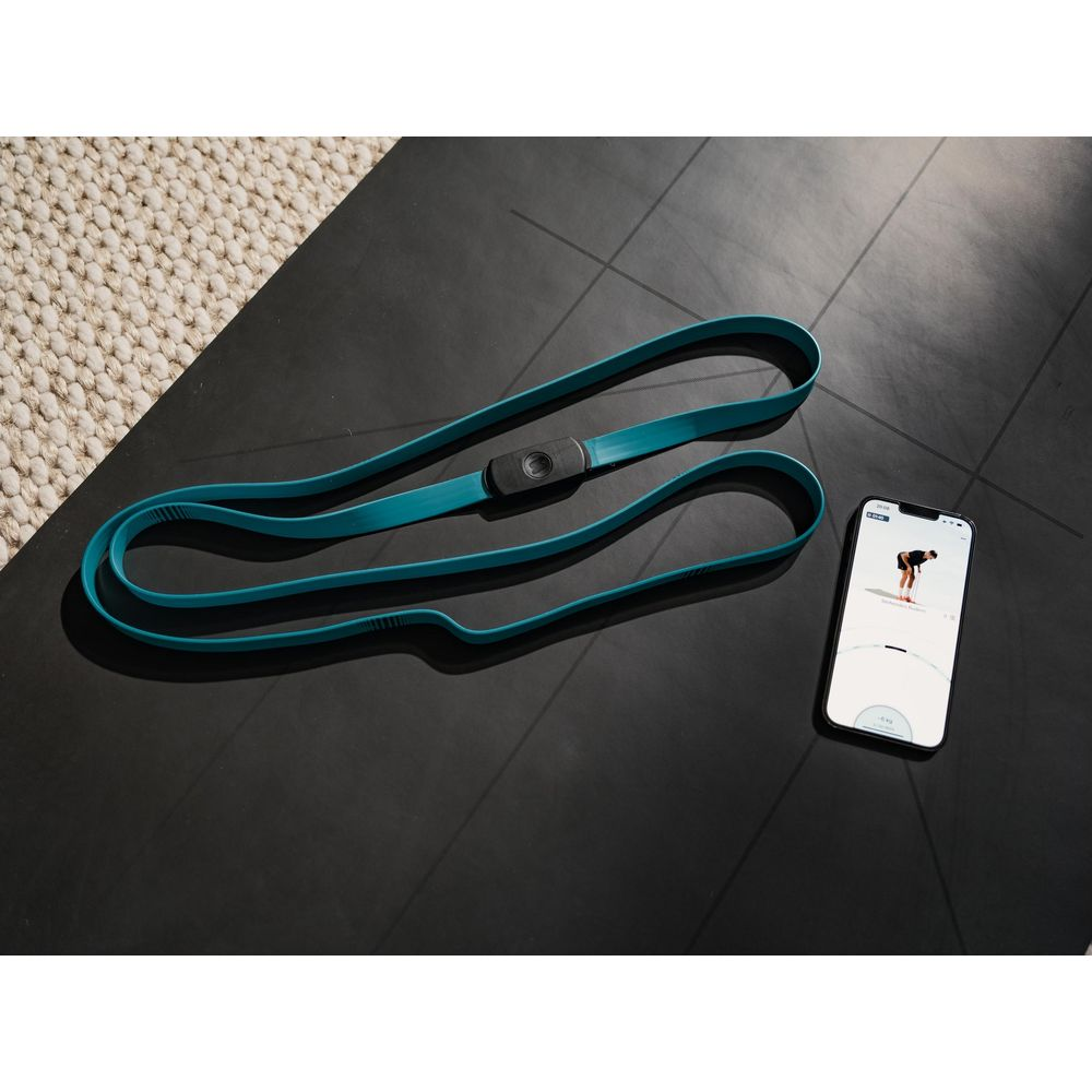 Un élastique bleu sarcelle est posé à côté d'un smartphone sur un tapis noir.