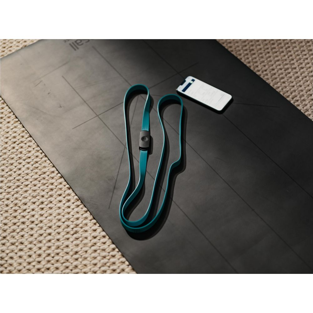 Un élastique turquoise avec capteur noir repose sur un tapis de yoga noir.