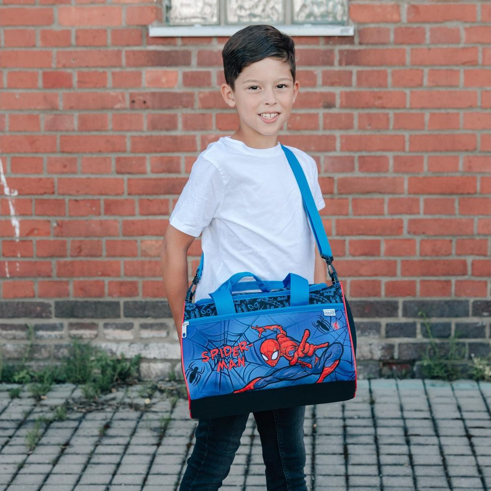 Ein Junge mit einer Spiderman-Tasche steht vor einer Ziegelwand.