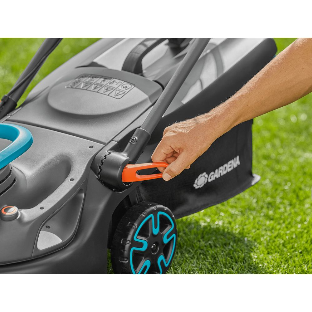 Hand betätigt orangefarbenen Hebel an einem Rasenmäher auf grünem Gras.