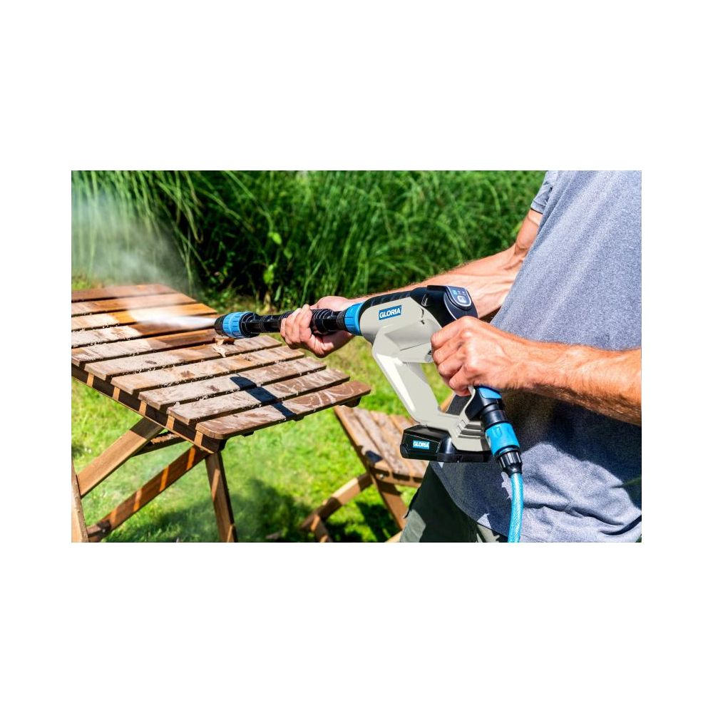 Mann reinigt Holztisch mit Hochdruckreiniger im Garten.