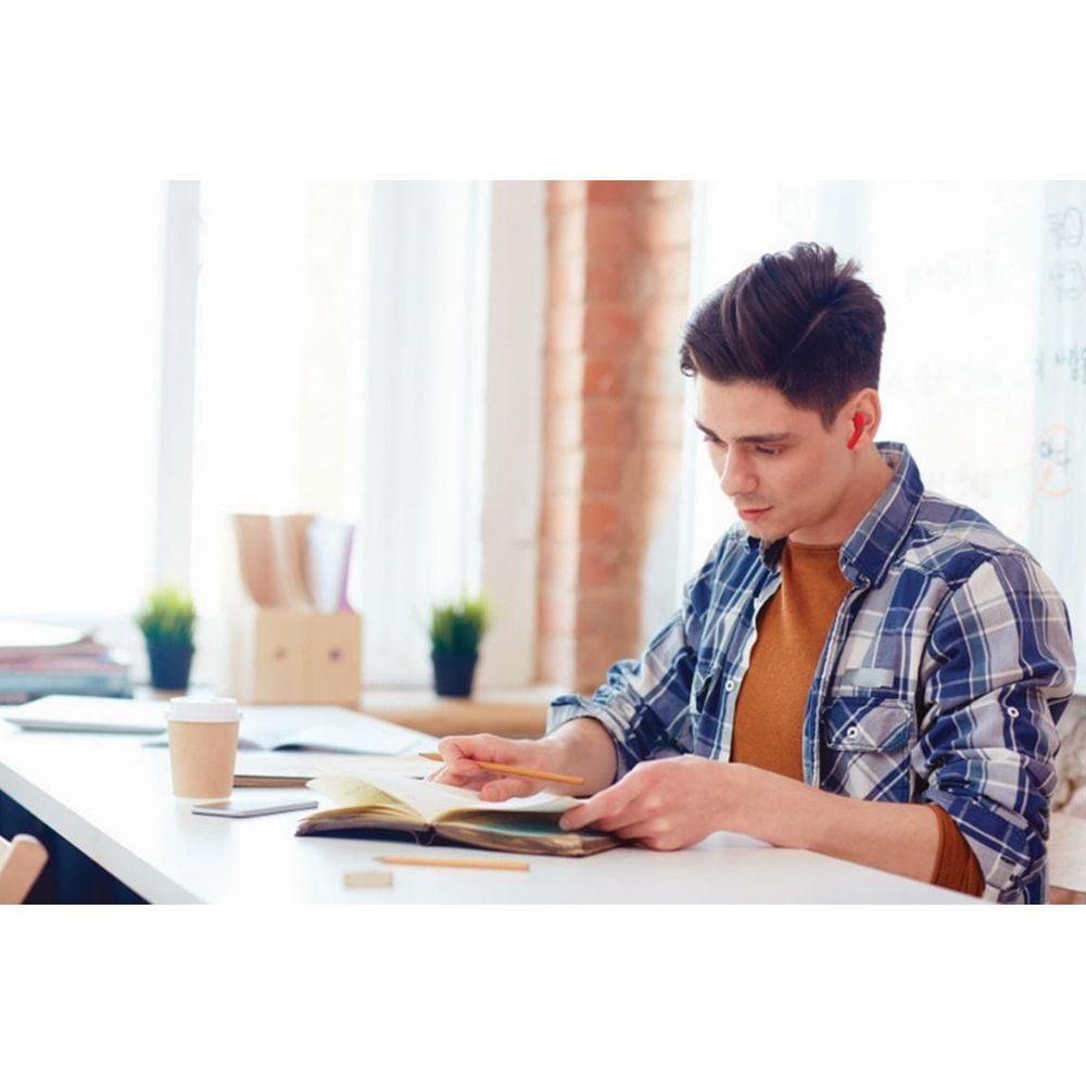 Joven con audífonos estudia en un escritorio con cuaderno y bolígrafo.