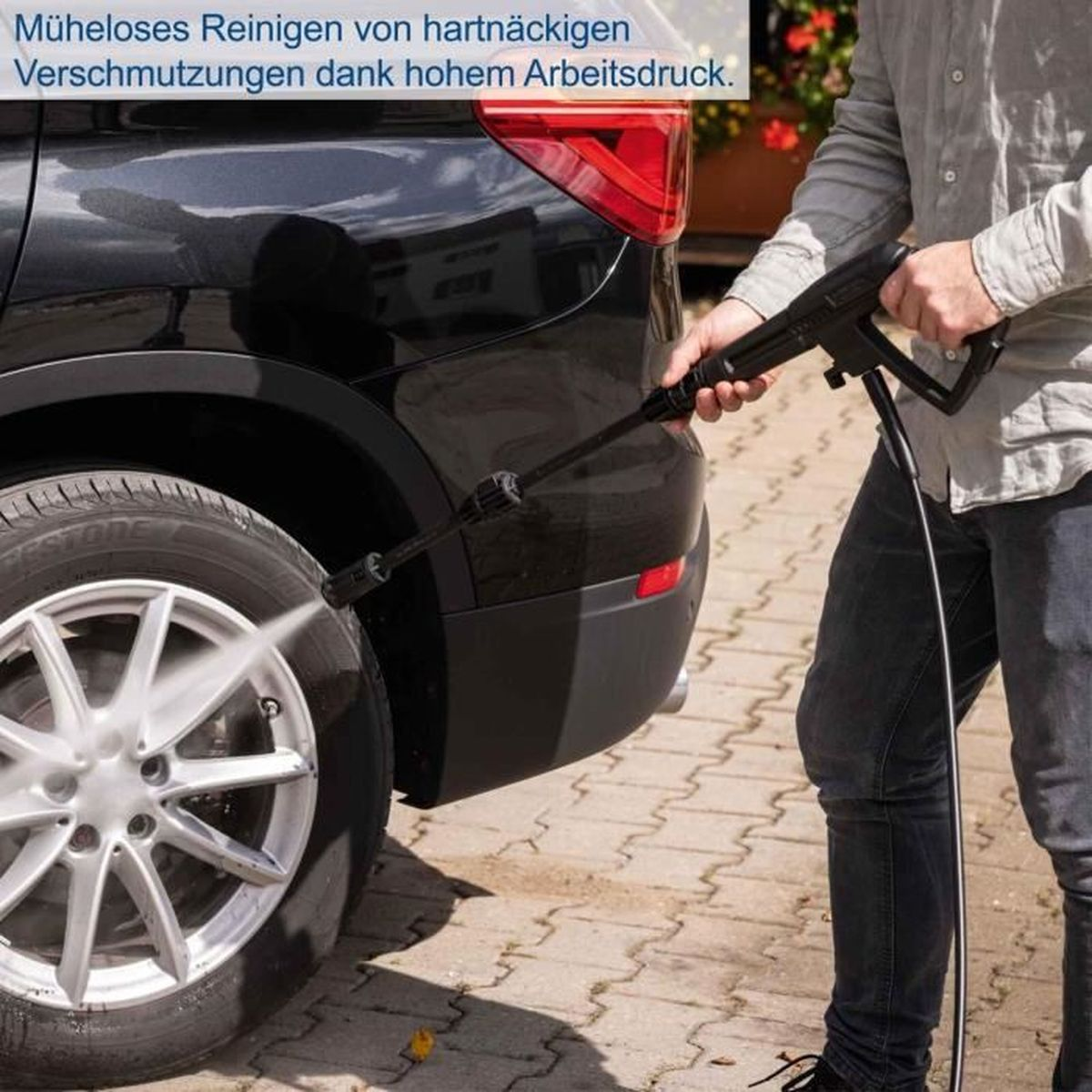 Osoba czyści samochód myjką ciśnieniową przy kole.