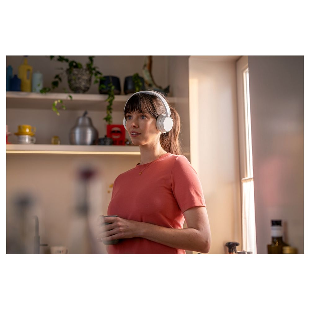 Eine Frau mit weißen Kopfhörern und einem Korall-T-Shirt hält eine Tasse.