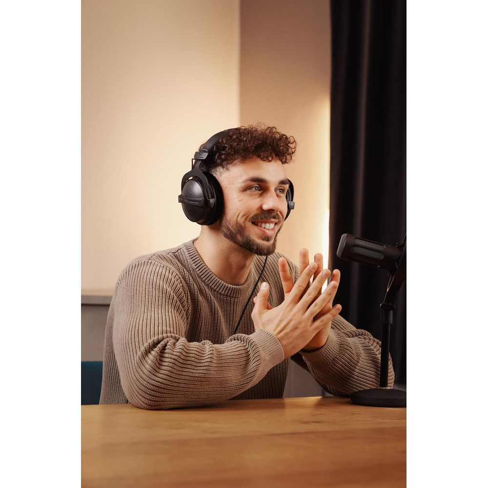 Mężczyzna w słuchawkach siedzi przy stole i mówi do mikrofonu.