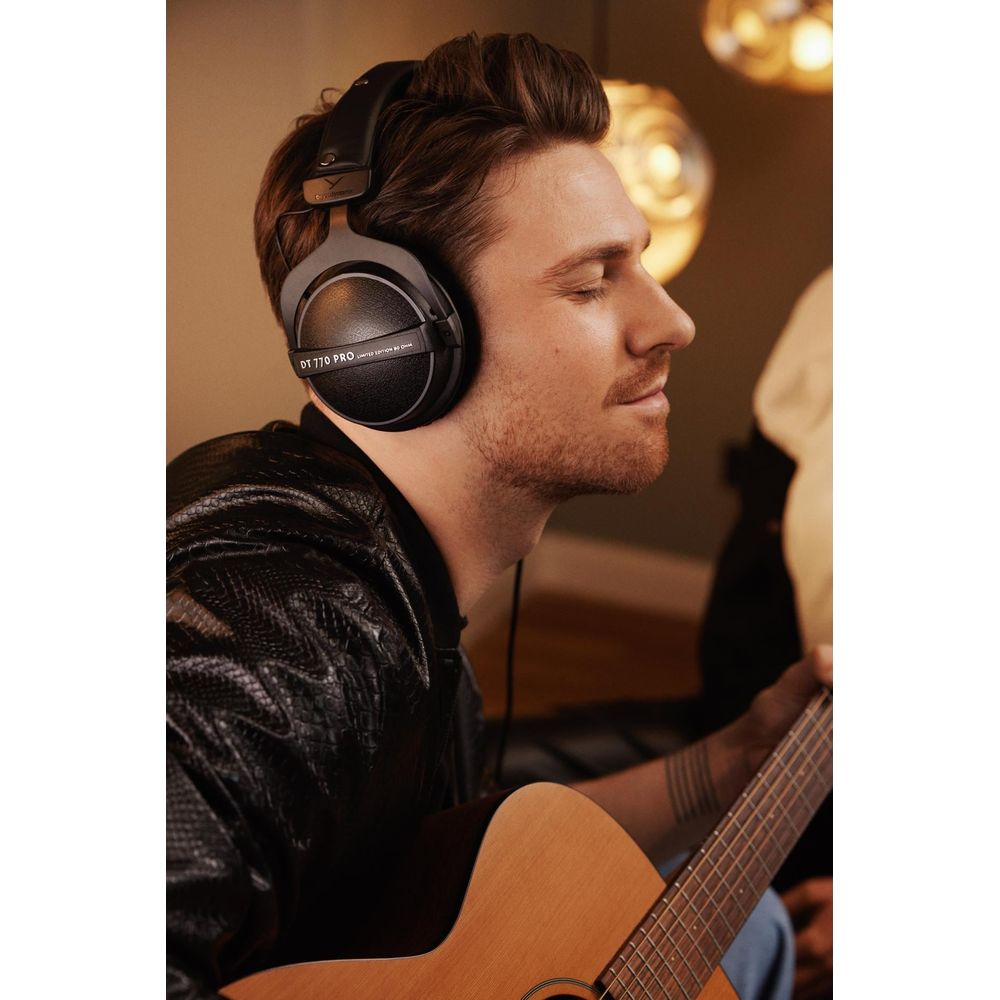 Mężczyzna w słuchawkach gra na gitarze, oczy zamknięte.