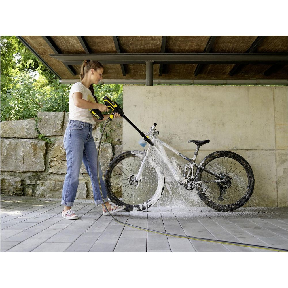 Una donna pulisce una bicicletta con idropulitrice su una superficie pavimentata.