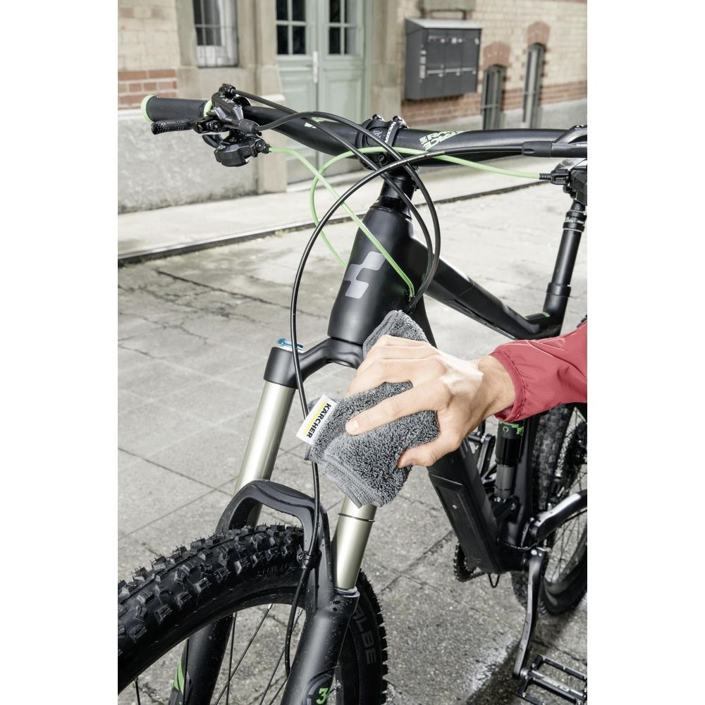 Persona pulisce telaio bici con panno grigio. Ruota anteriore e forcella visibili.