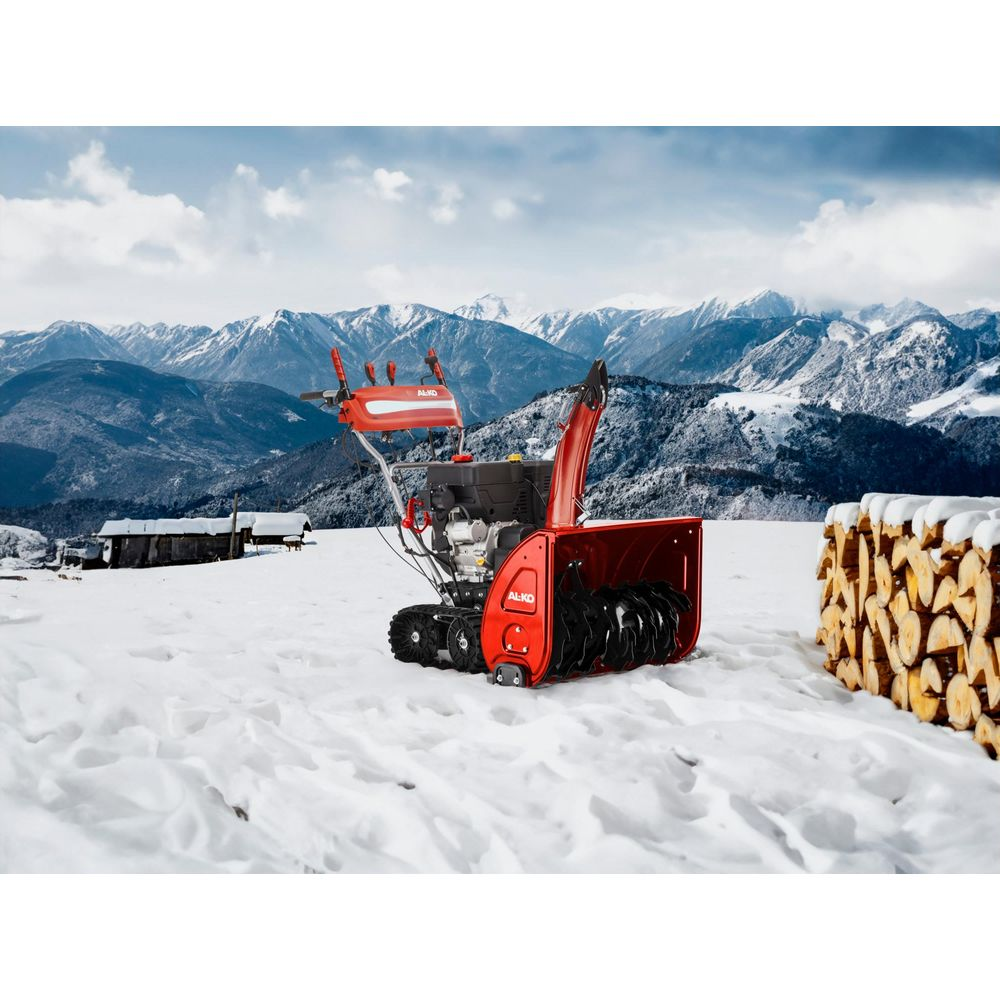 Ein roter Schneefräse steht im Schnee vor schneebedeckten Bergen.