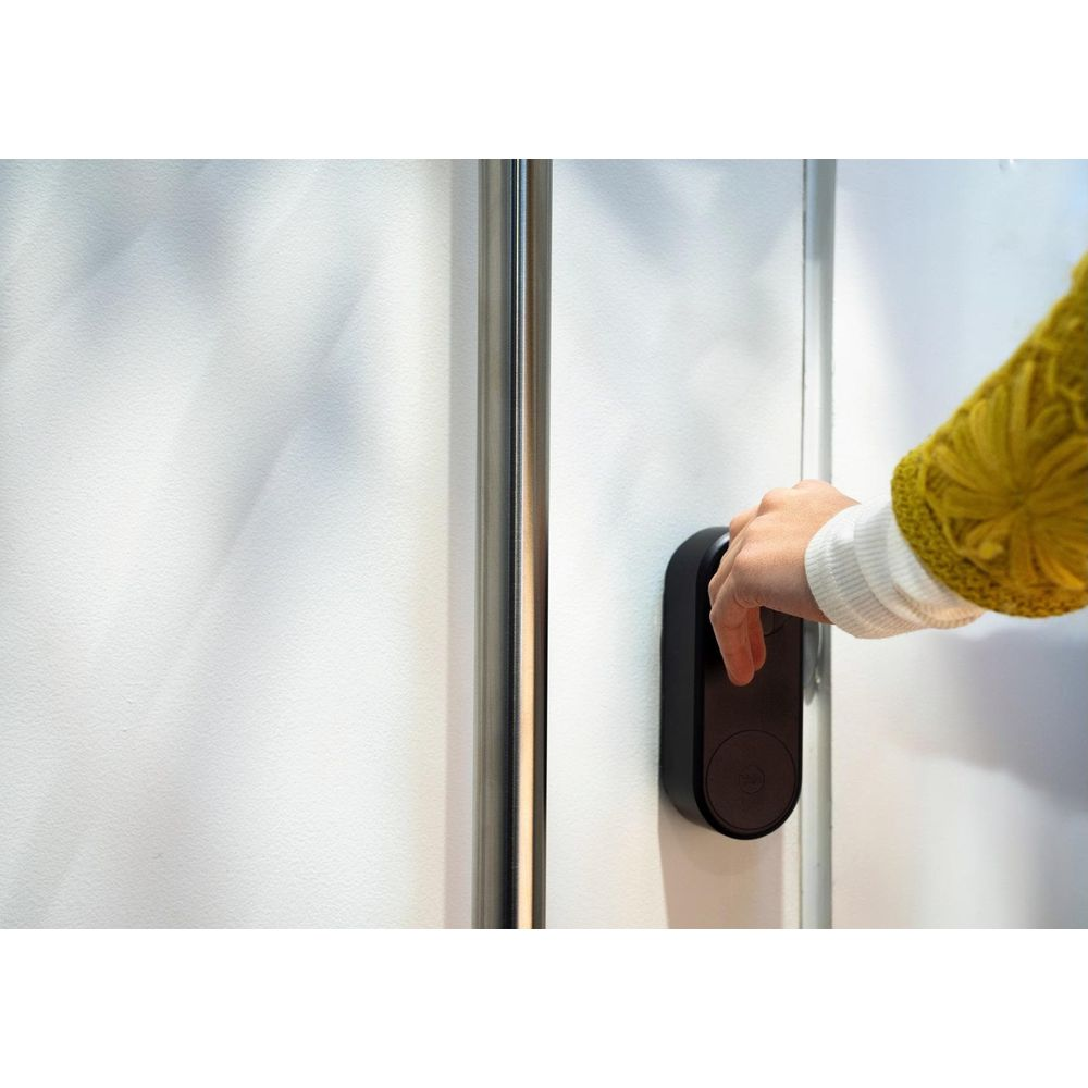 Eine Hand in einem gelben Pullover bedient ein schwarzes Smart Lock an einer weißen Tür.