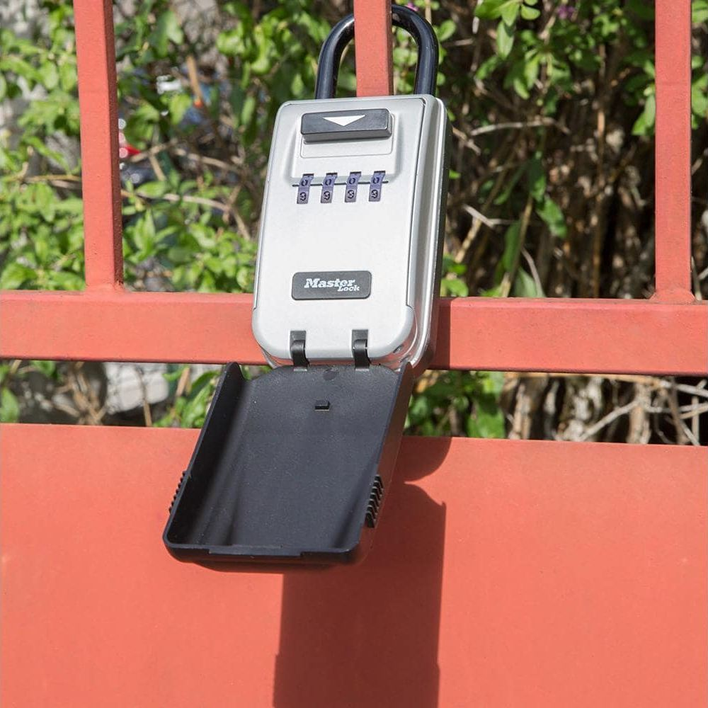 Un portachiavi a combinazione argentato con la porta aperta è appeso a una recinzione rossa.