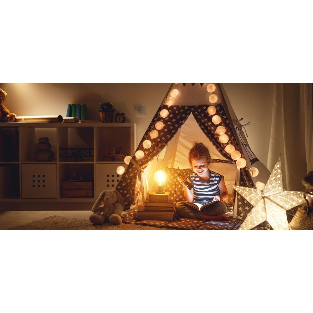Une fille lit dans une tente éclairée, entourée de jouets et de décorations étoiles.