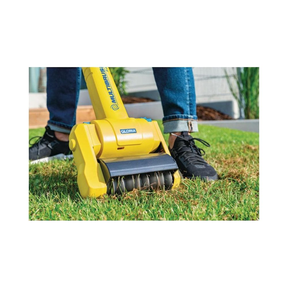 Żółty aerator do trawy z obrotowymi szczotkami na zielonej trawie, osoba w jeansach.