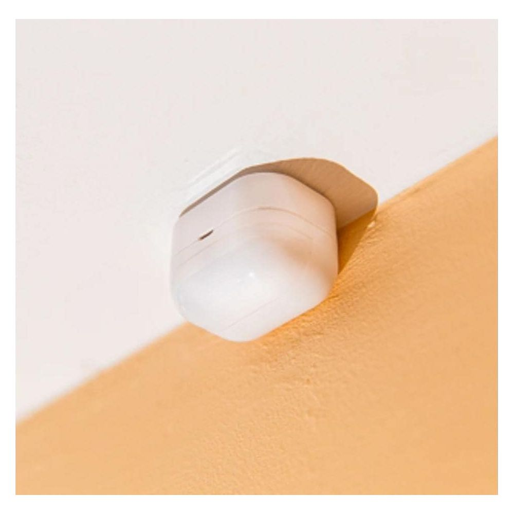 Białe etui ładujące do bezprzewodowych słuchawek spoczywa na pomarańczowej ścianie.