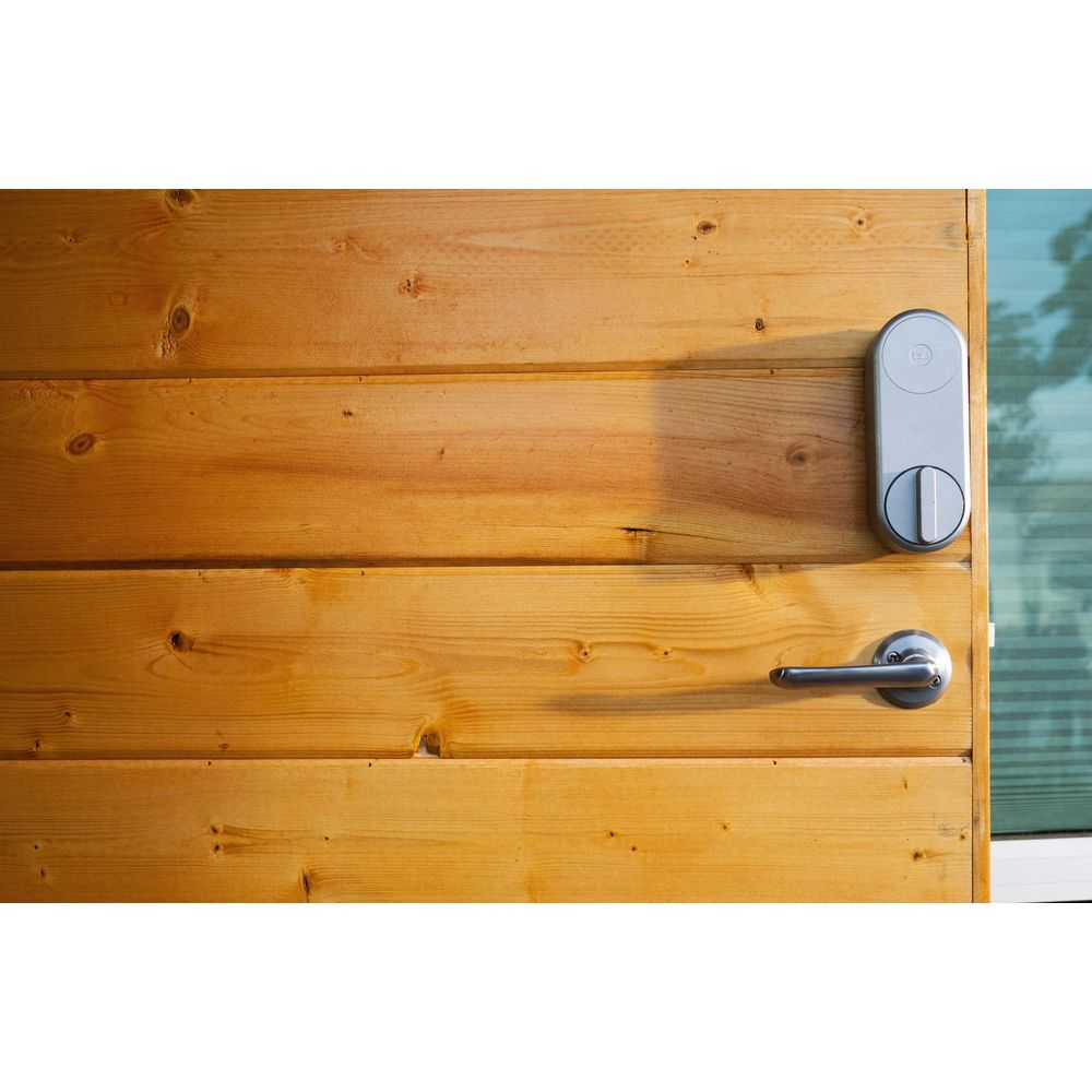 Srebrna inteligentna klamka i zamek na drewnianych drzwiach. Słońce rzuca cień.