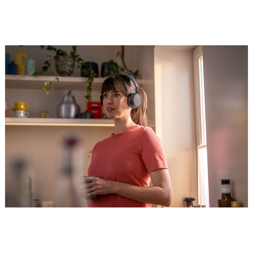 Mujer con auriculares y taza, estantes de cocina al fondo.