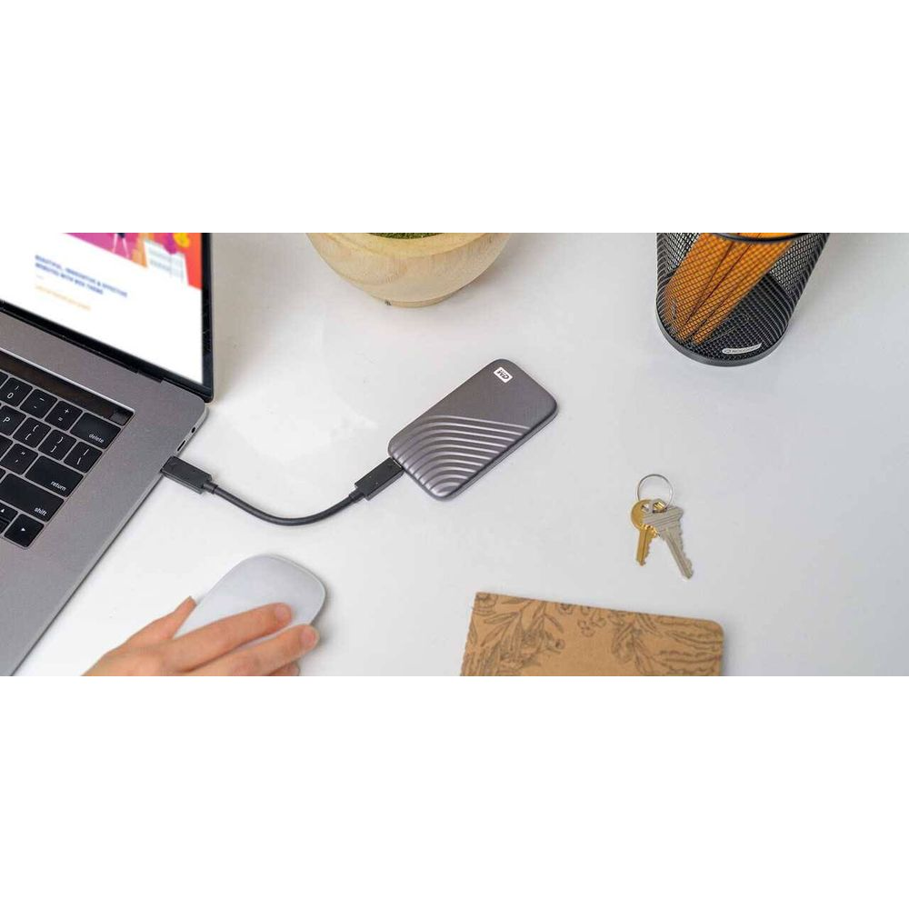 Szary dysk zewnętrzny podłączony do laptopa i myszy, klucze w pobliżu.