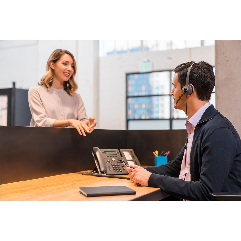 Hombre con auriculares hablando con mujer en escritorio con teléfono.