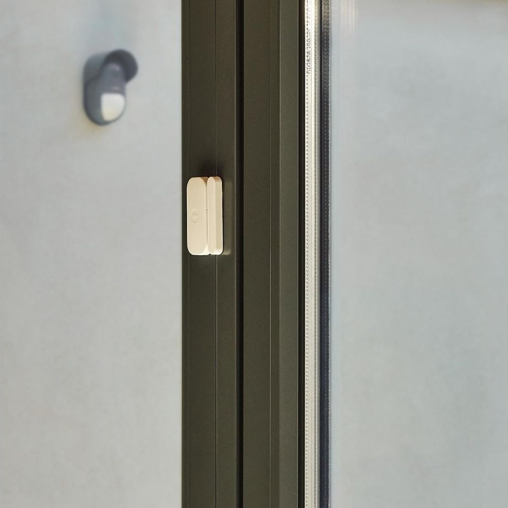 Un sensore bianco porta/finestra è su un telaio scuro. Un sensore grigio è sul muro.