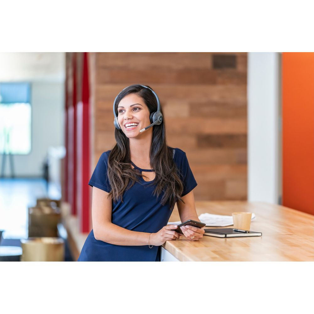 Kobieta w zestawie słuchawkowym opiera się o lada, trzymając telefon.