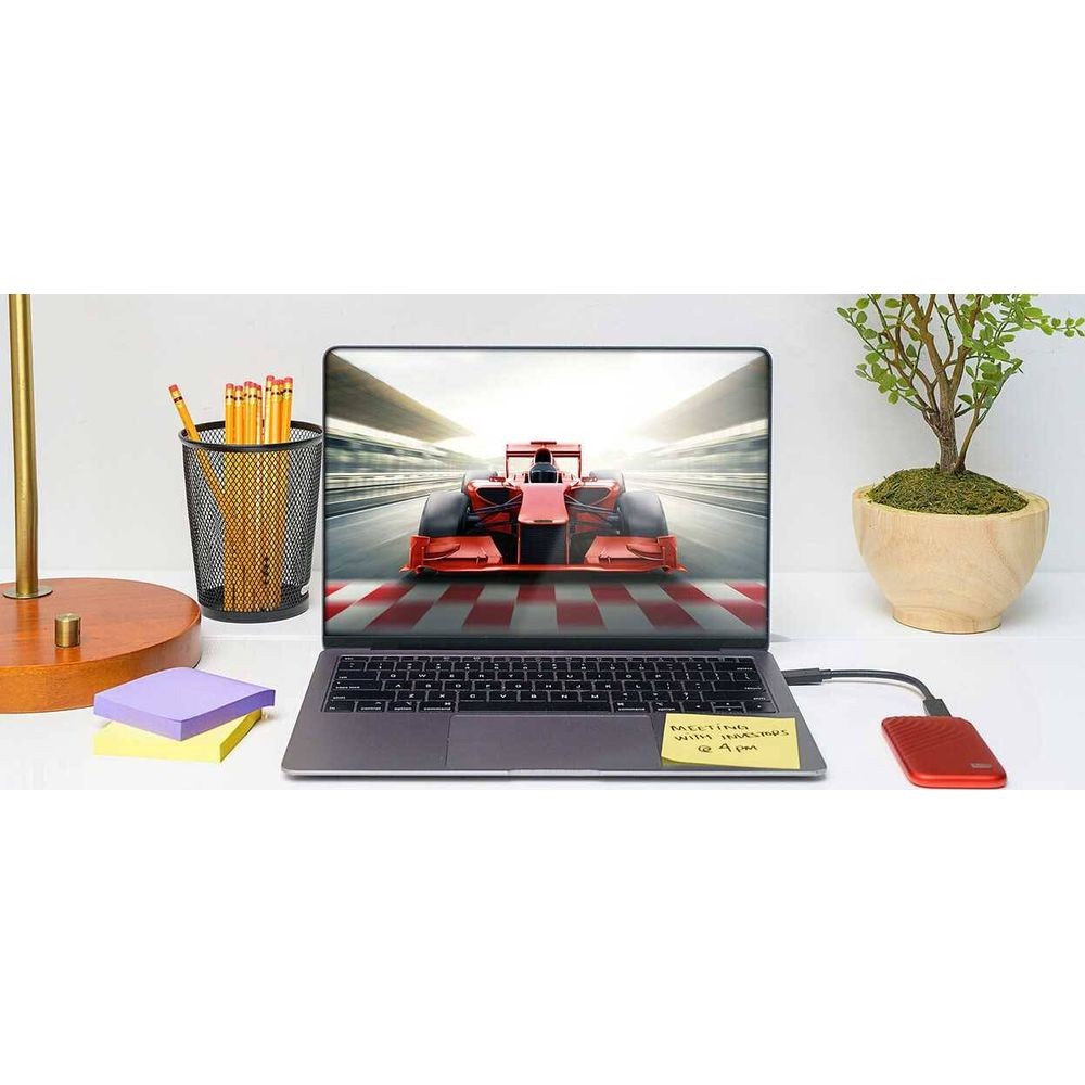 Laptop wyświetla czerwony bolid F1 na torze. Biurko z ołówkami, notatkami, rośliną.