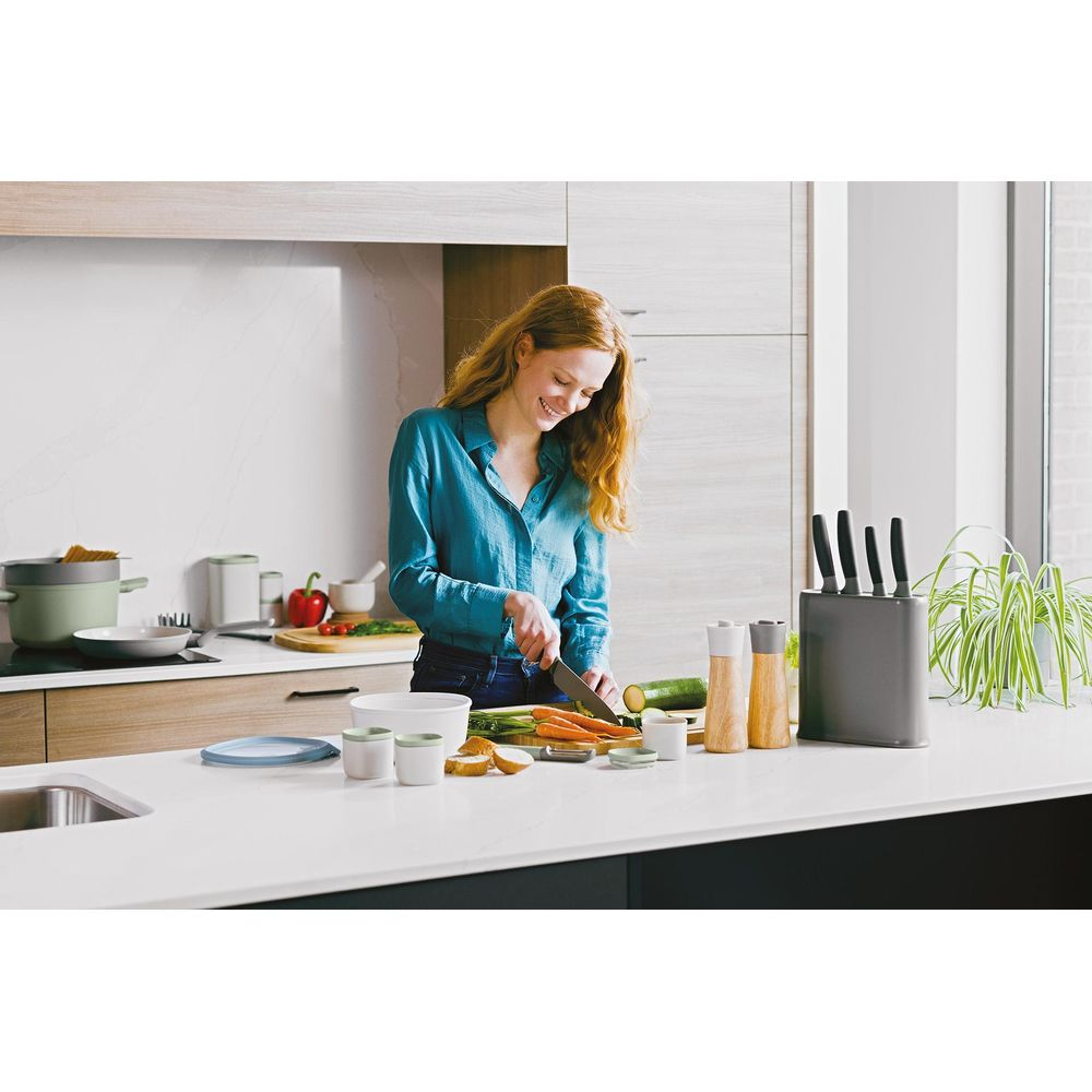 A woman is cutting vegetables with a knife in a modern kitchen.