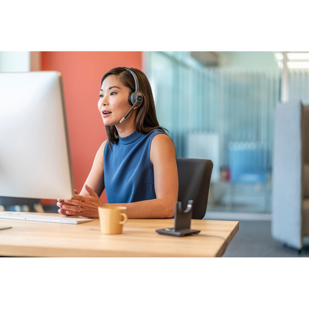 Eine Frau mit Headset sitzt am Schreibtisch und blickt auf einen Monitor.