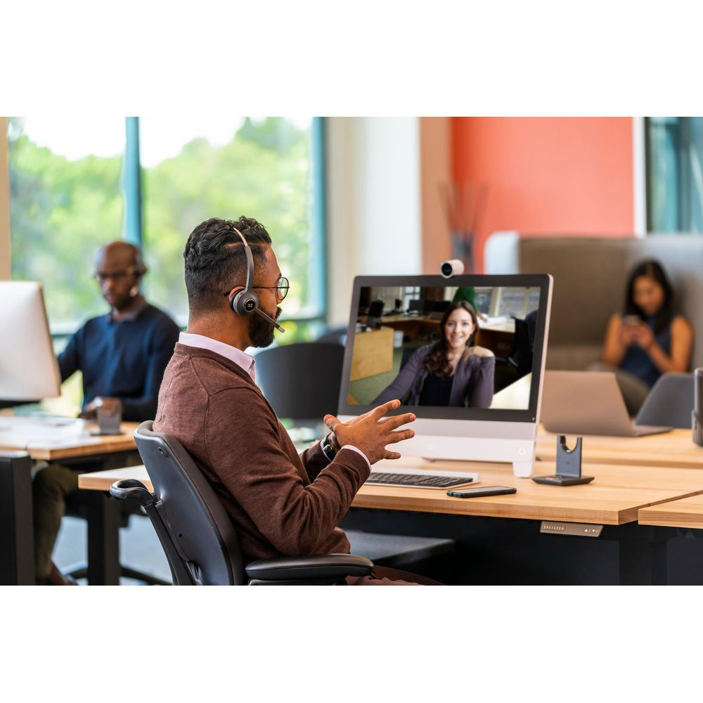 Mann mit Headset telefoniert am Computer mit Kollegin. Büroumgebung.