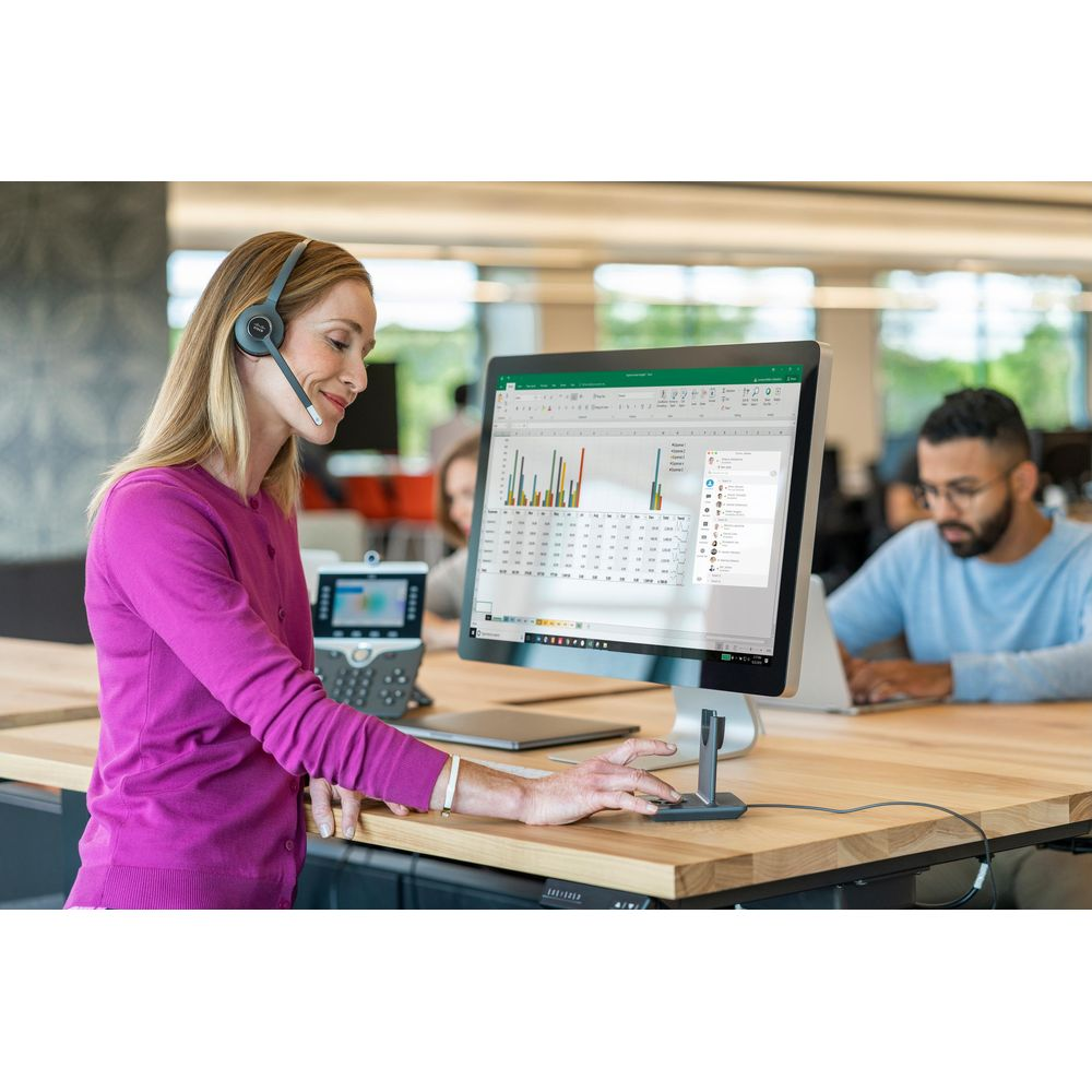 Frau mit Headset arbeitet am Computer. Im Hintergrund ein Mann.