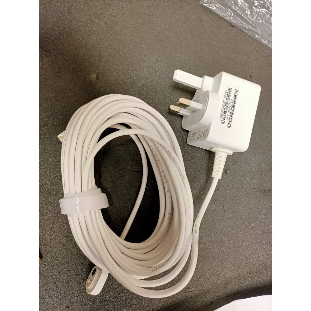 Ein weißer britischer Netzadapter mit einem aufgewickelten weißen Kabel liegt auf dunkler Oberfläche.
