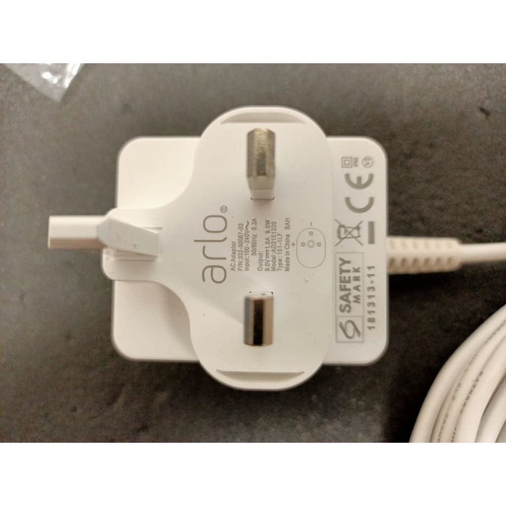 Ein weißer Arlo AC-Adapter mit drei Stiften und CE- und Safety Mark-Zertifizierungen.