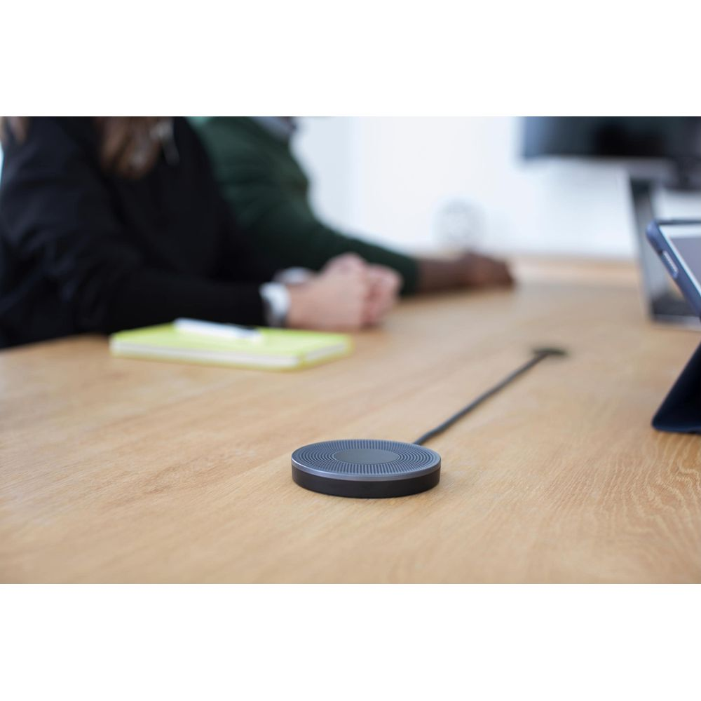 Een zwarte microfoon op een houten tafel, met mensen op de achtergrond.