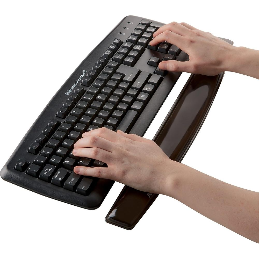 Manos escribiendo en un teclado negro con reposamuñecas marrón.