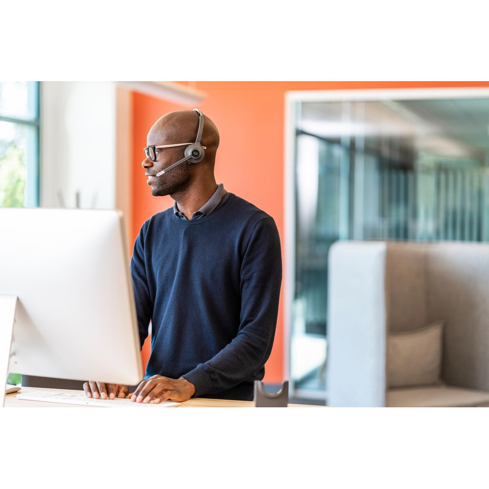 Mężczyzna w słuchawkach siedzi przy komputerze w granatowym swetrze.