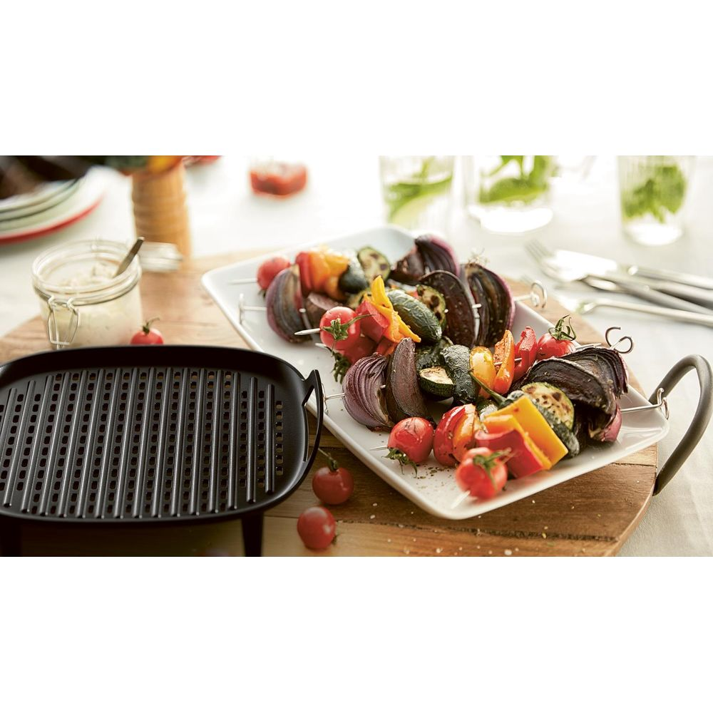 Padella grill con spiedini di verdure, pomodori e salsa su tavolo.