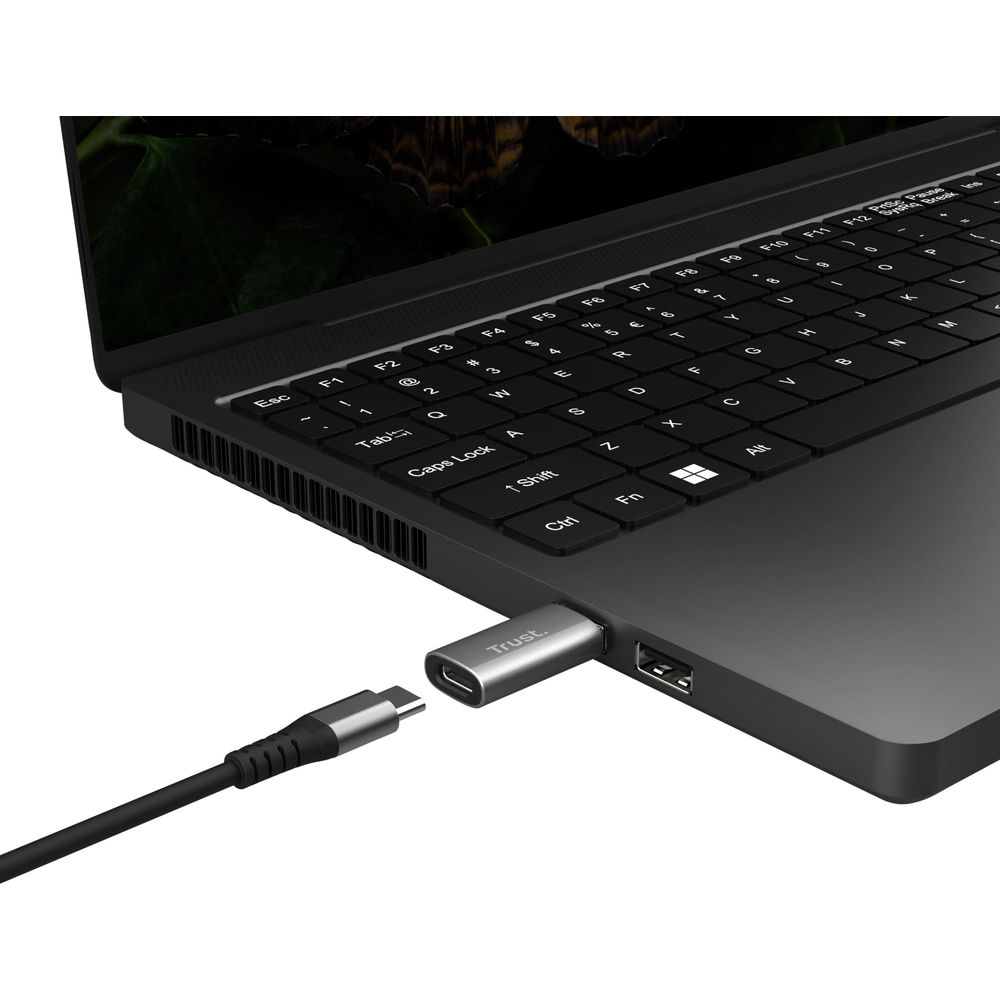 Kabel USB-C łączy się z srebrnym adapterem Trust podłączonym do laptopa.