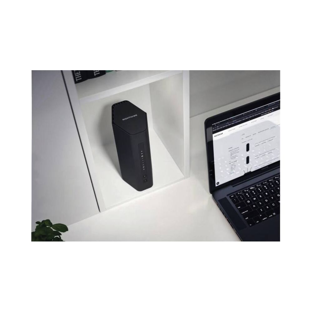 Czarny router na półce obok otwartego laptopa.