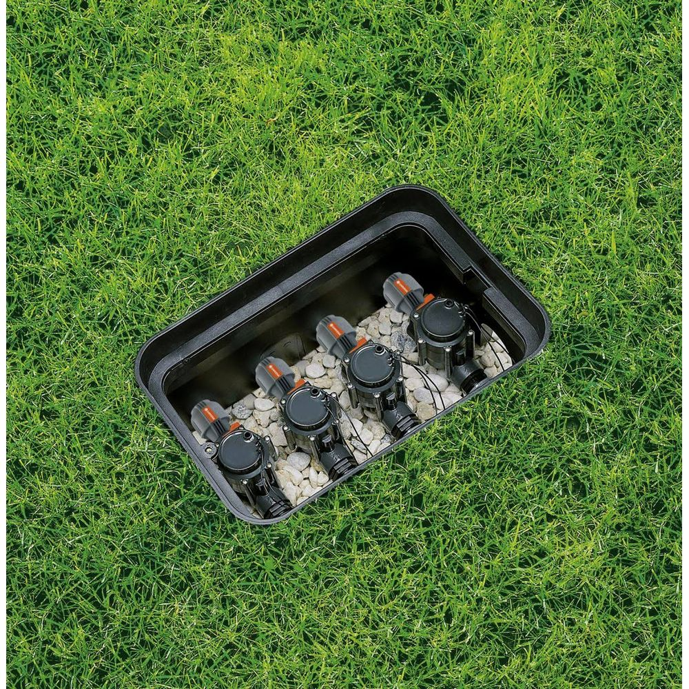 Ein schwarzer Bewässerungsverteiler mit vier Ventilen in einem Grasgarten.