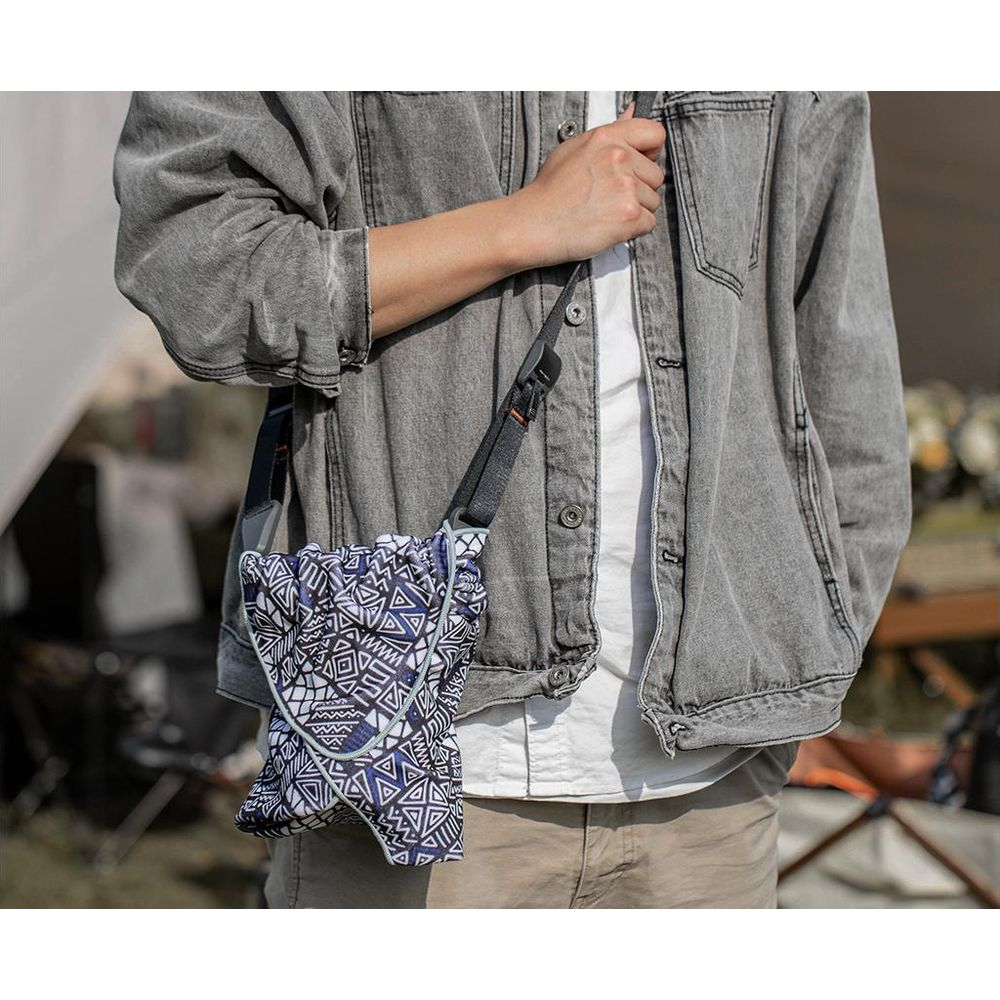 Person mit grauem Jeanshemd und Tasche mit geometrischem Muster.