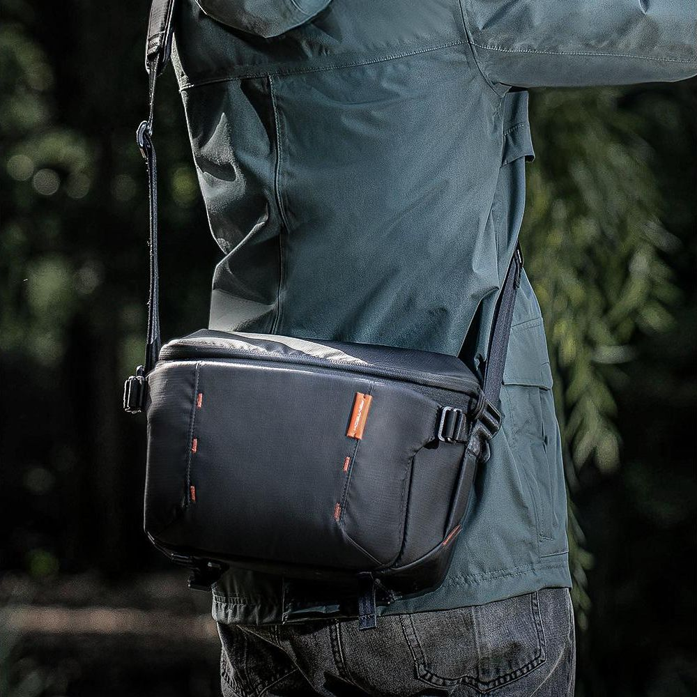 Persona con borsa a tracolla nera con accenti arancioni, all'aperto.