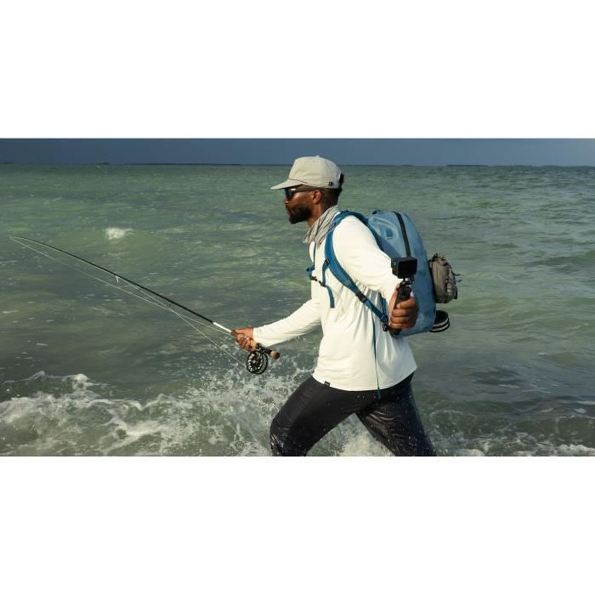 Un hombre en el agua pesca con una caña, llevando una mochila.