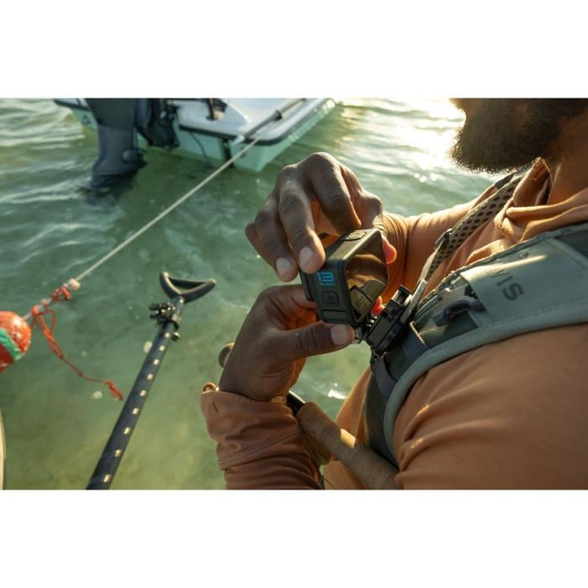 Hombre se pone GoPro en chaleco sobre el agua con bote y remo al fondo.