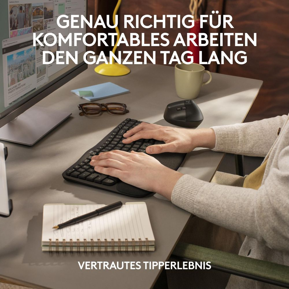 Una persona escribe en un teclado, al lado de un ratón vertical, gafas y cuaderno.